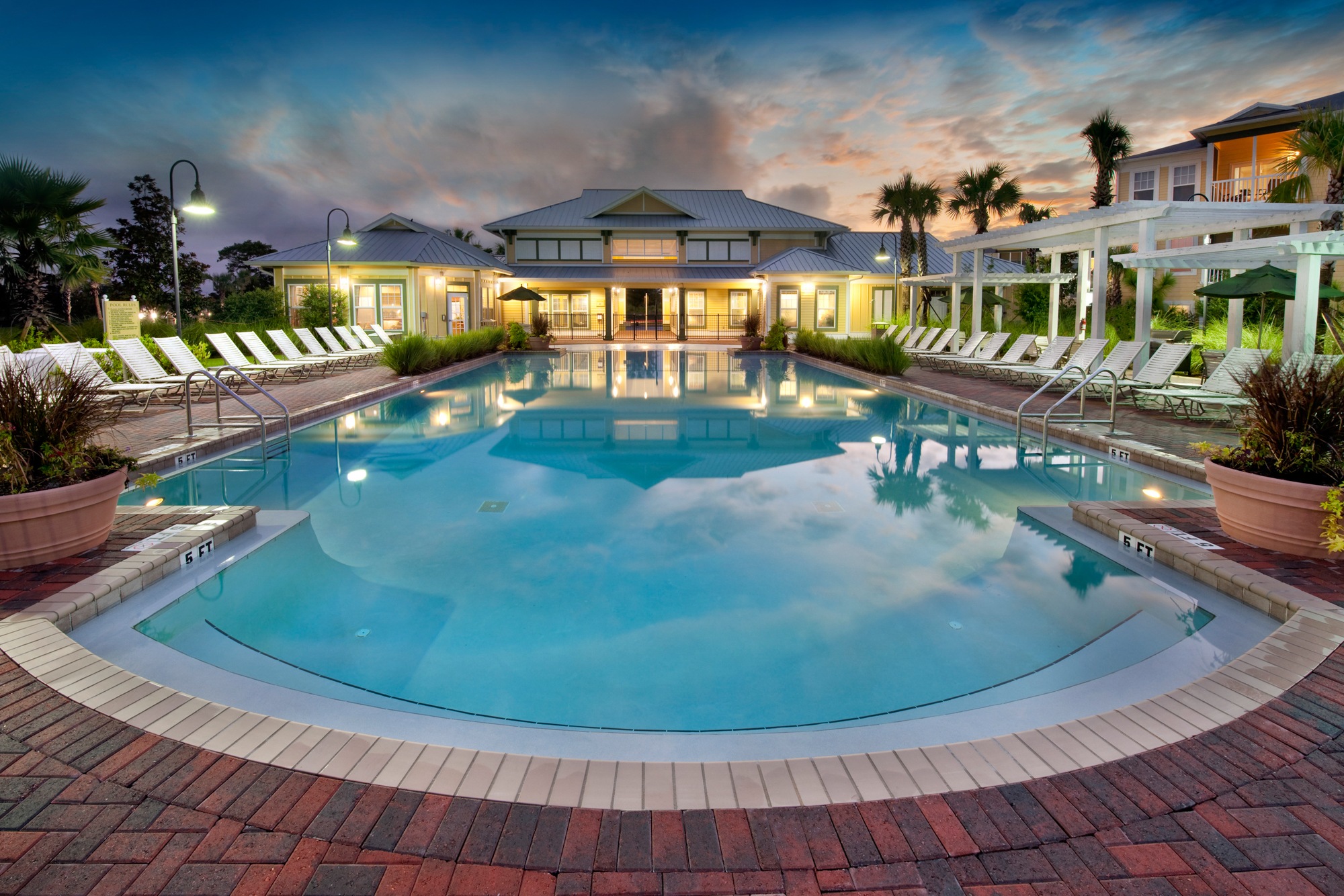 A large outdoor swimming pool surrounded by a brick patio and lounge chairs.